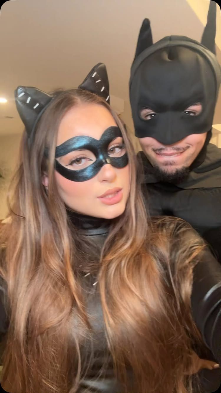 Couple wearing black cat and Batman costumes posing for a close-up selfie.