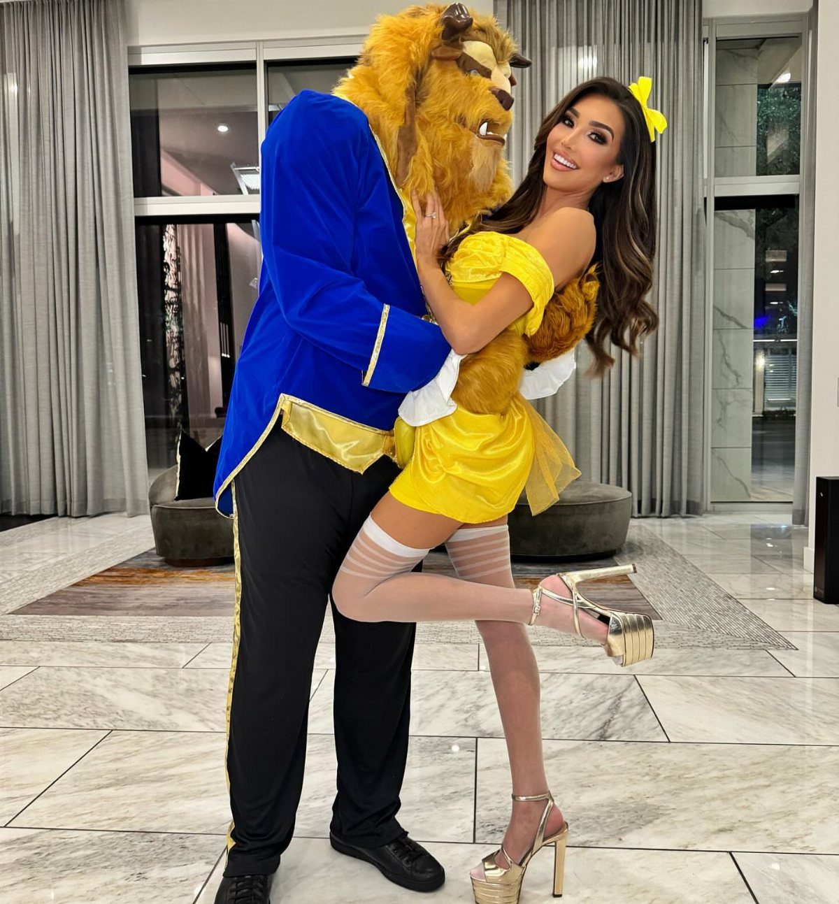 Couple dressed as Beauty and the Beast posing in a modern living room.