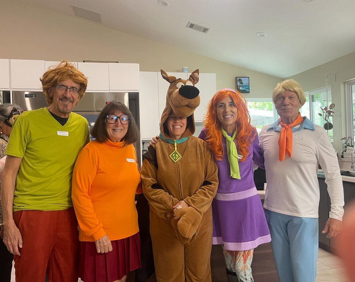 Five adults dressed as the Scooby-Doo gang posing together in a kitchen.