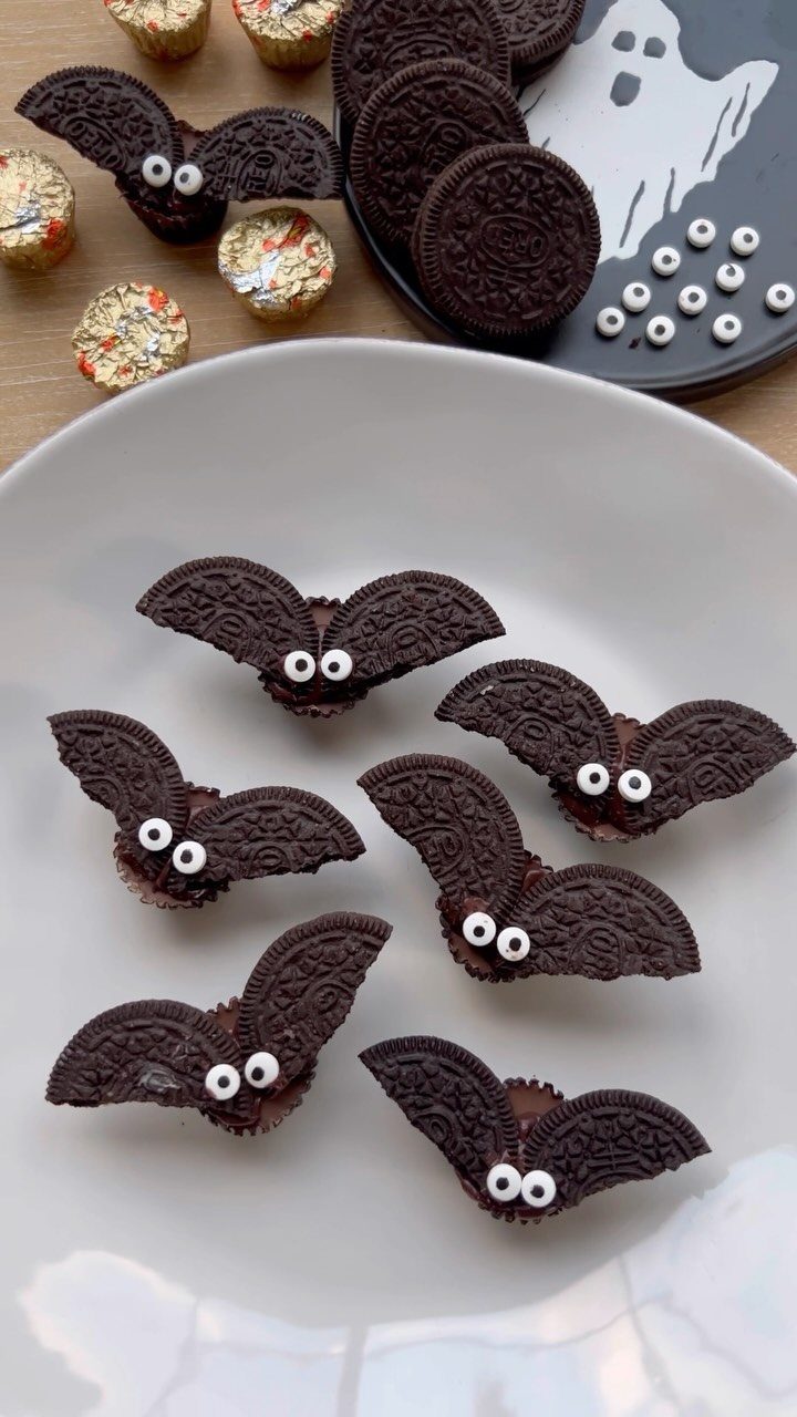 Bat-shaped chocolate cupcakes with cookie wings and candy eyes on a white plate.