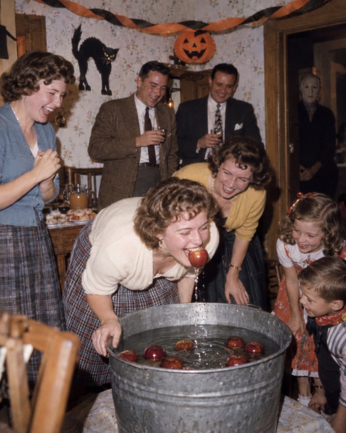 Woman bobbing for red apples in a metal tub at a Halloween party.