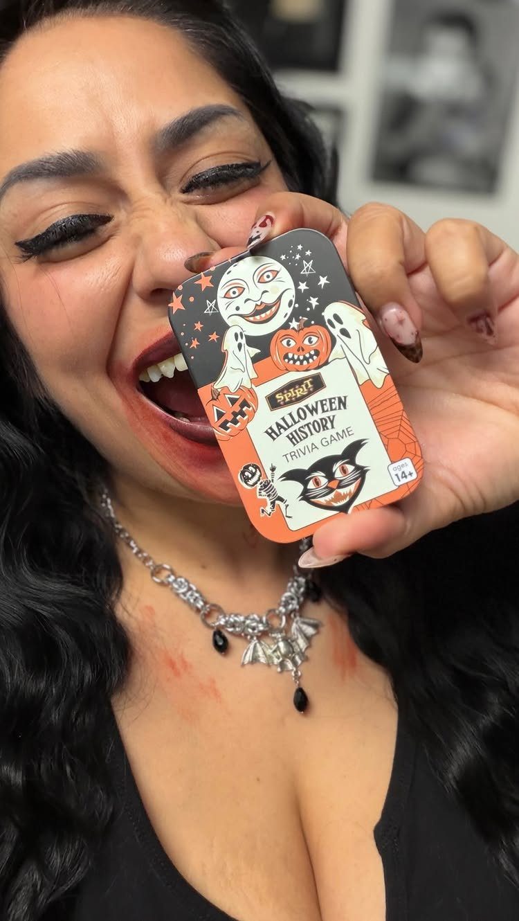 Woman with fake blood holding a Halloween History Trivia Game box near her face.