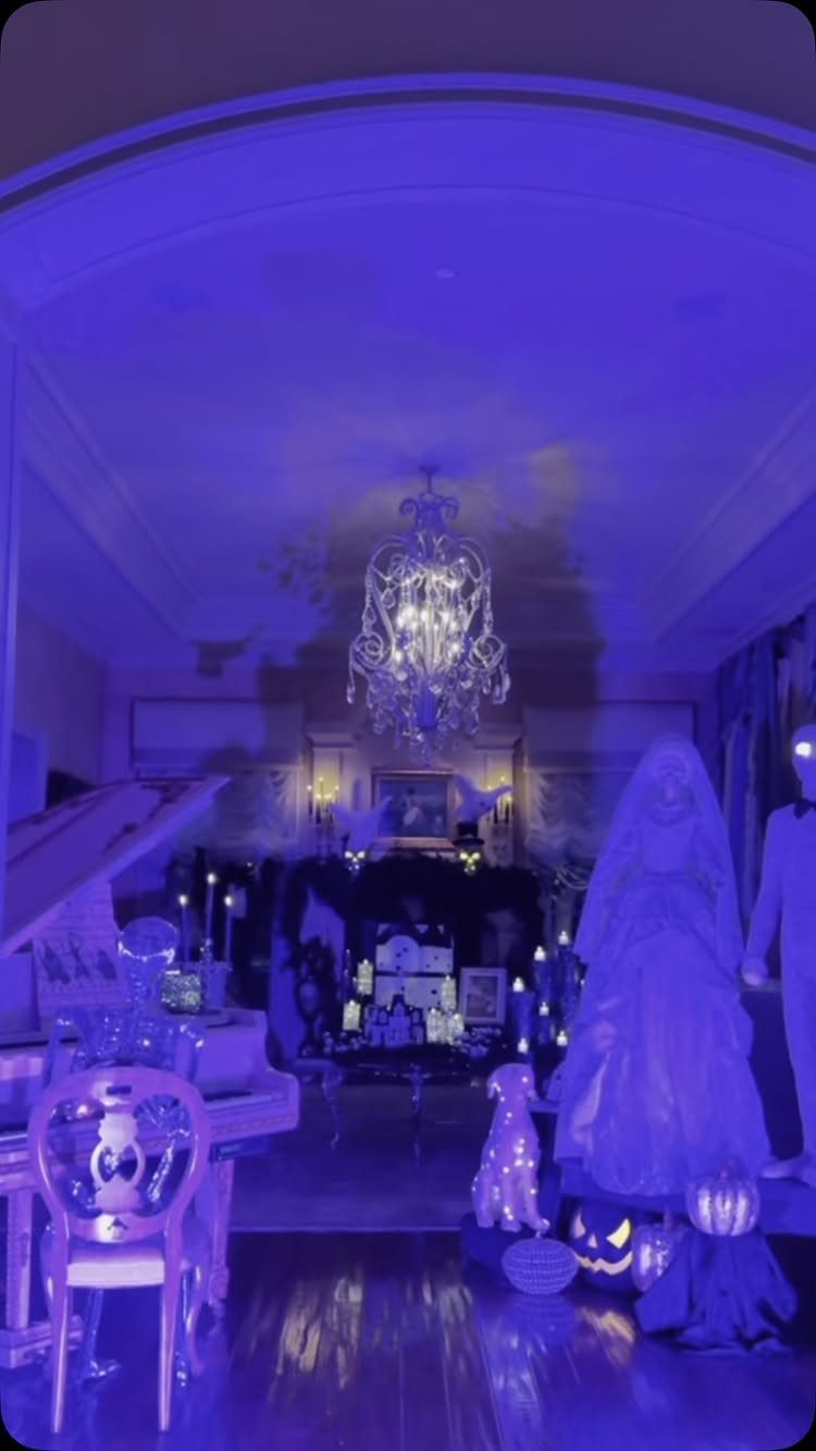 Purple lit room with a ghost figure, pumpkins, and a crystal chandelier.