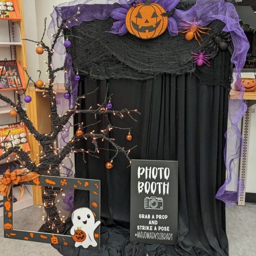 Halloween photo booth with black curtains, purple tulle, spooky tree, and themed props.
