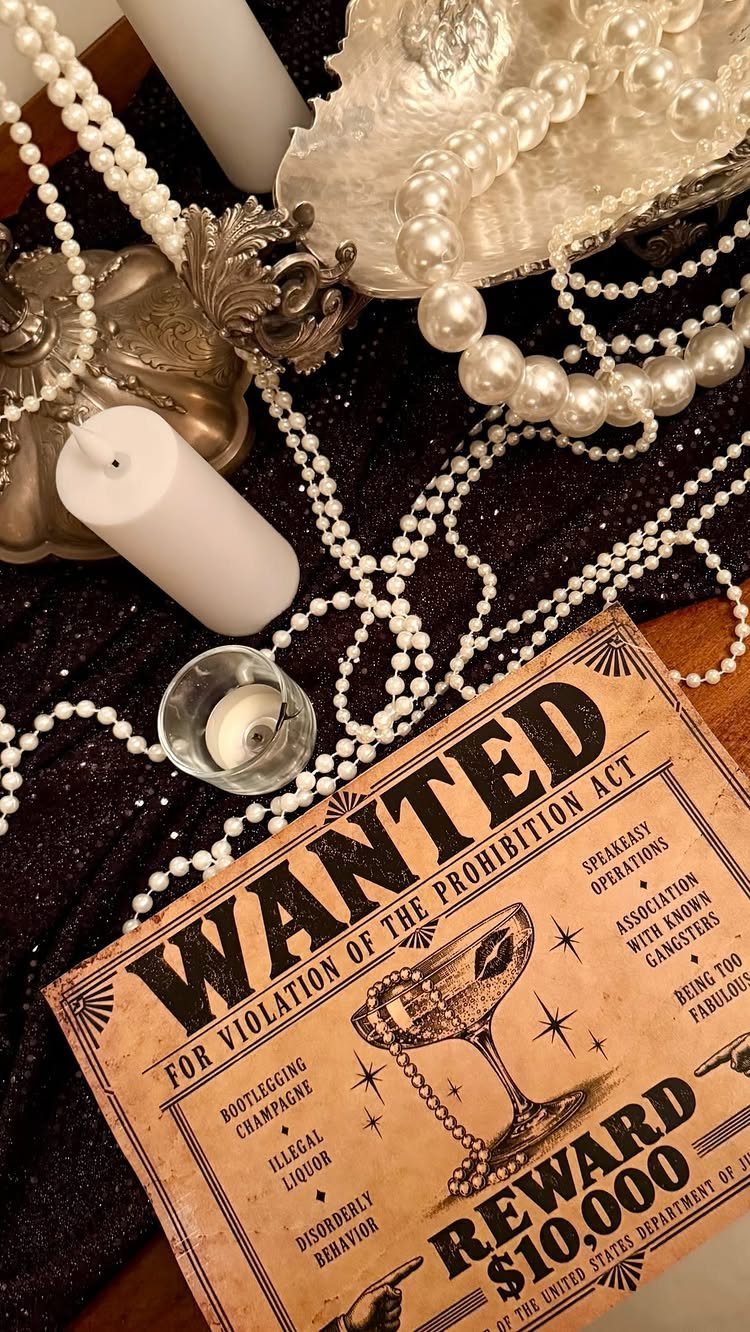 Vintage wanted poster, pearl necklaces, and white candles on a black glittery background.