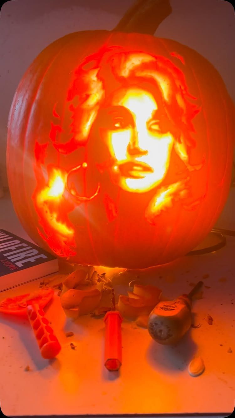 Carved pumpkin featuring a detailed woman's portrait illuminated from inside with carving tools.