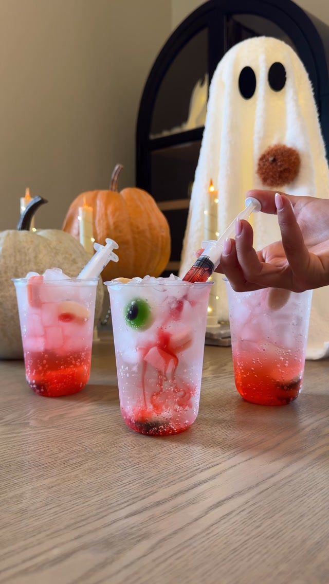 Spooky red cocktails with syringes and olives on a table with pumpkins.