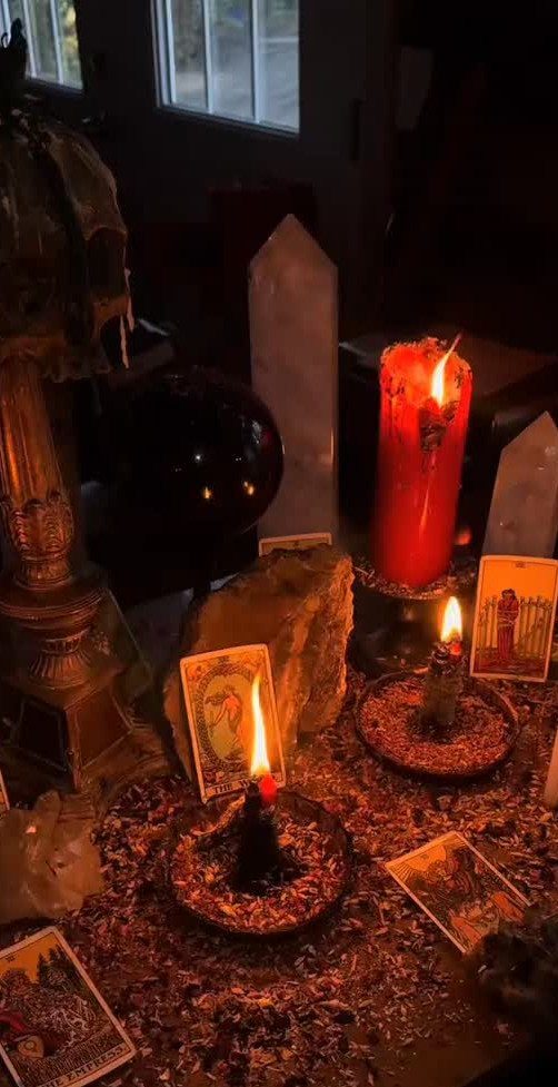Occult table setup with lit candles, tarot cards, crystals, and a black orb.