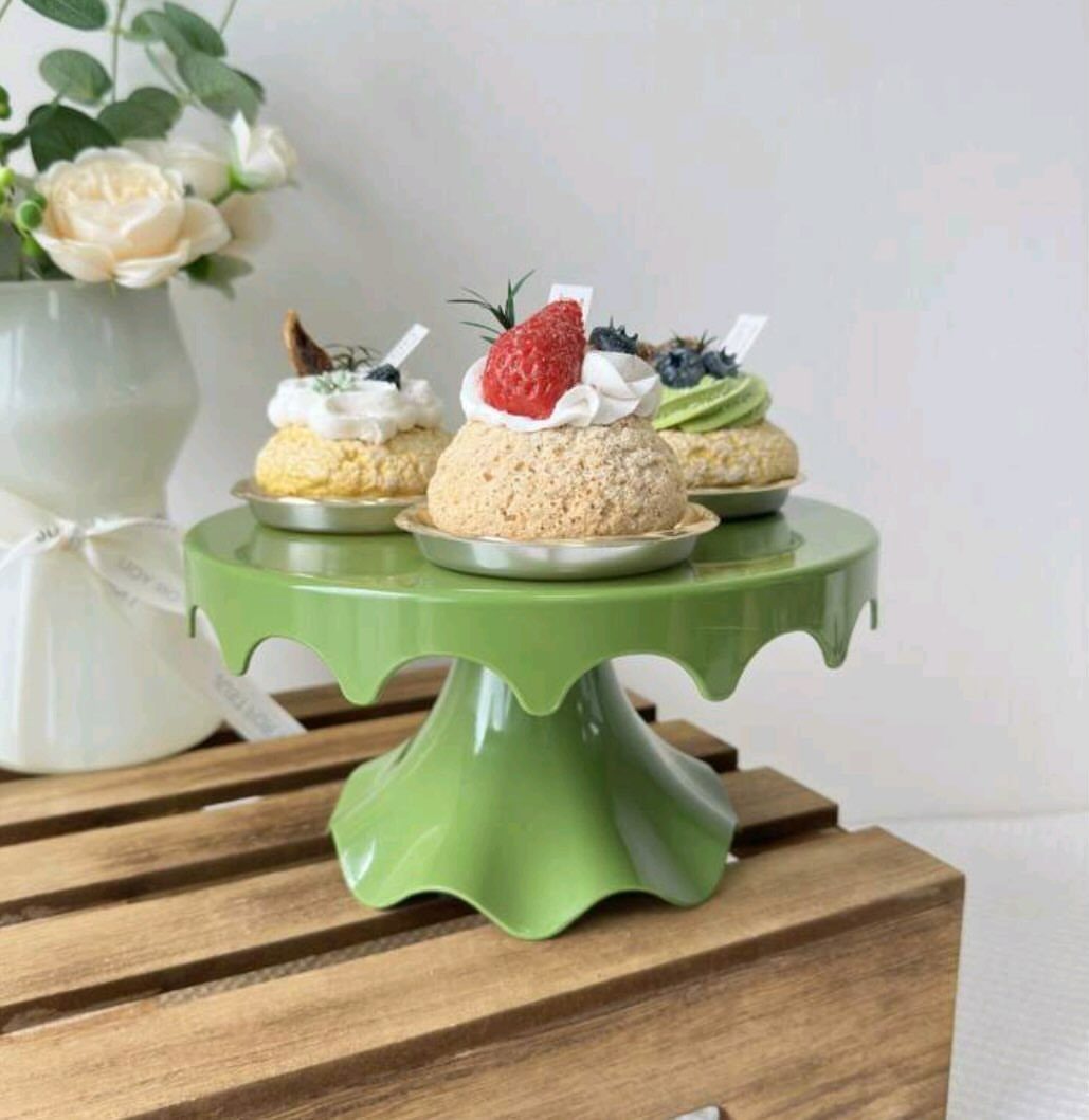 Light green cake stand holding three small berry cakes on a wooden surface