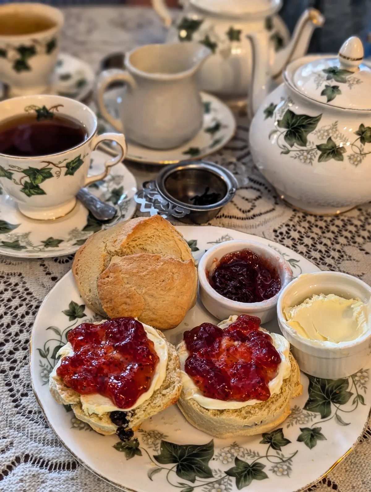 Scones topped with clotted cream and jam on an ivy-patterned tea plate.