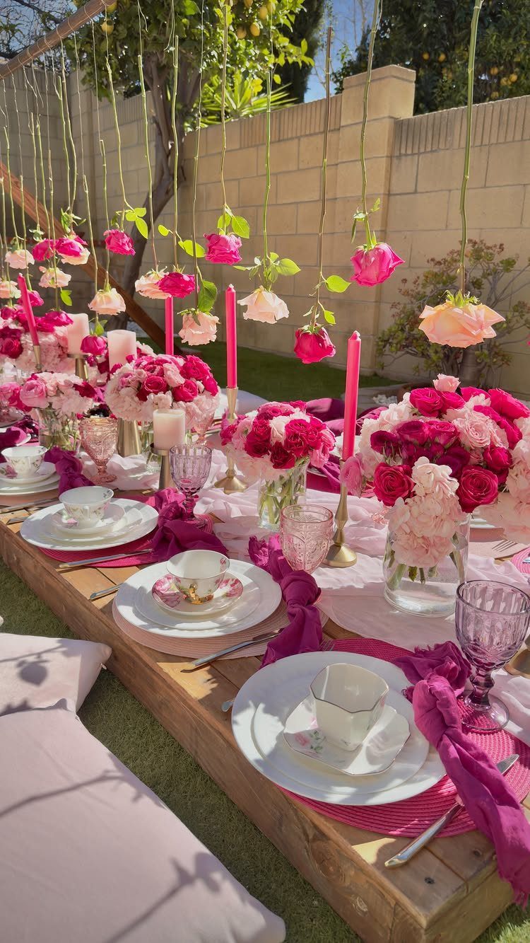 Low wooden table set for a tea party with pink flowers and hanging roses.