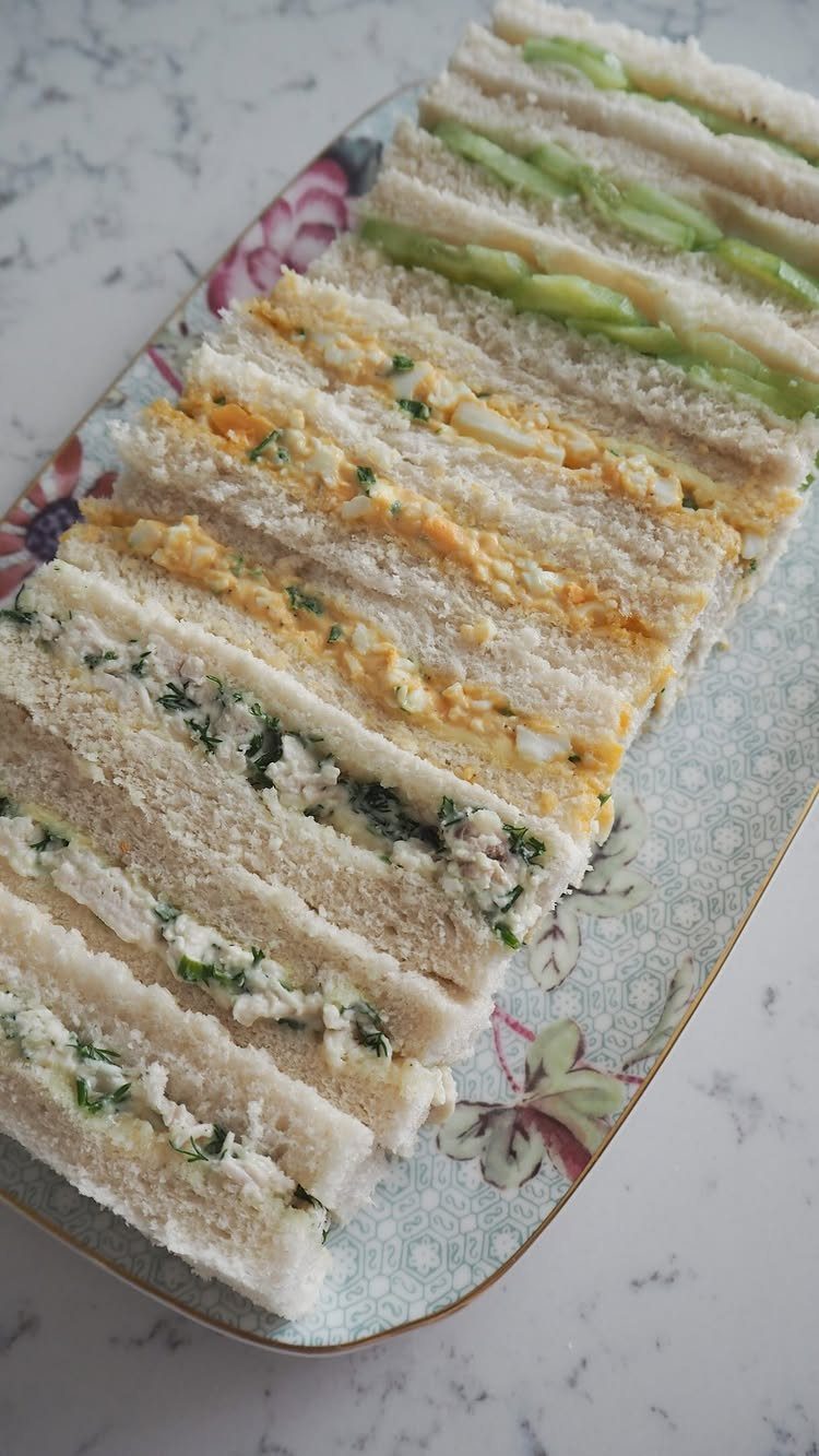 Assorted crustless finger sandwiches on a floral platter over a marble background.