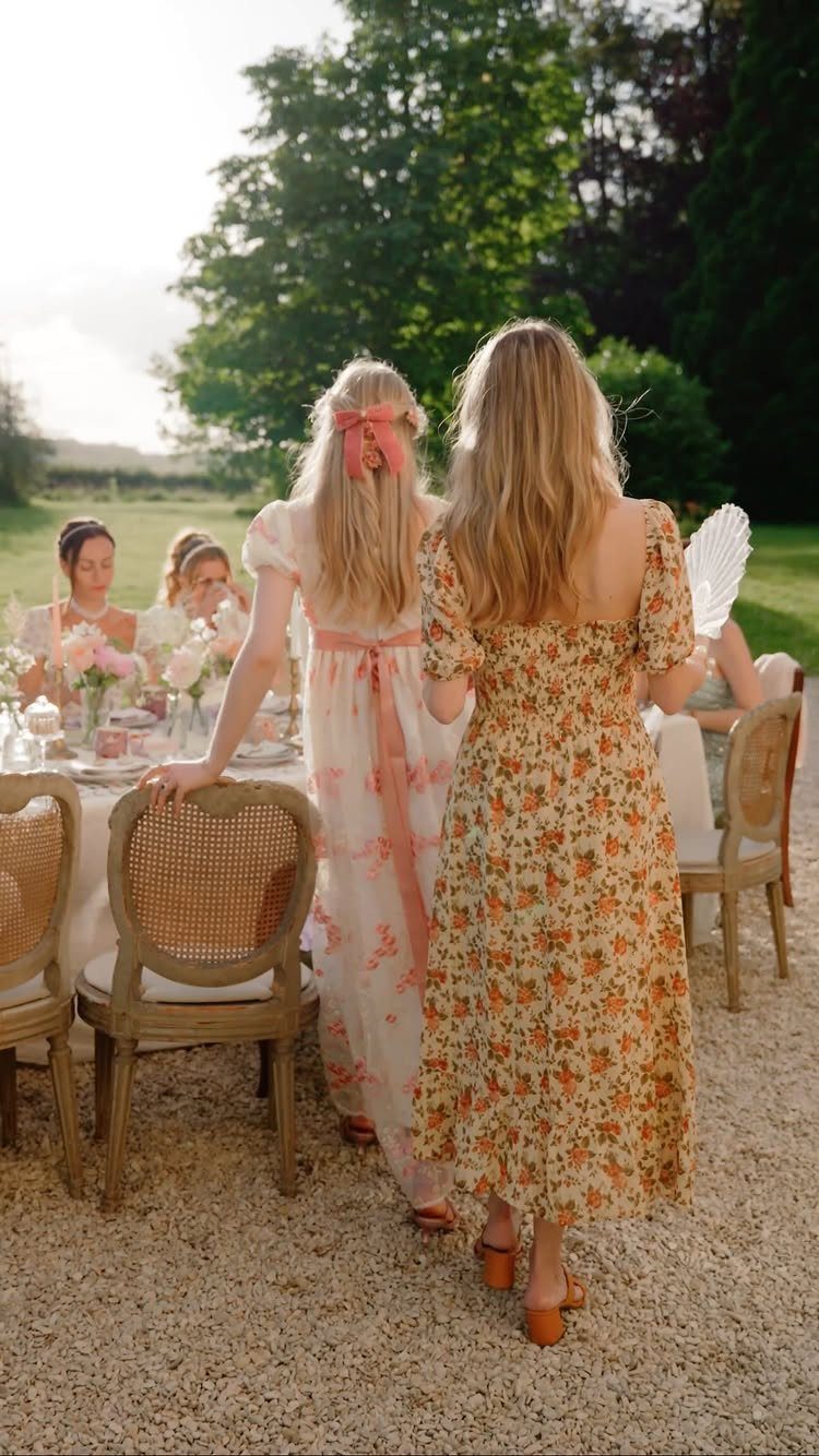 Women in floral dresses at an outdoor garden party with a decorated table.