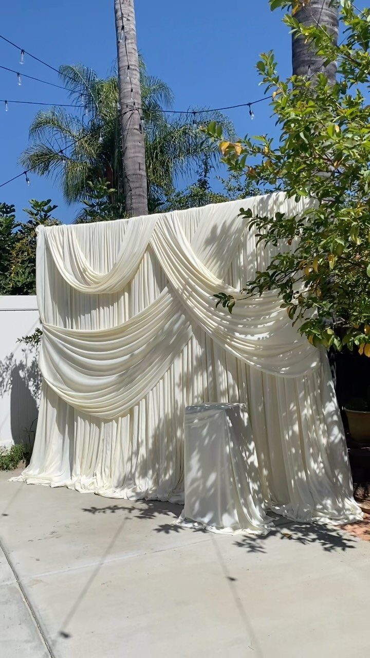 White draped fabric backdrop with elegant swags on an outdoor concrete patio.