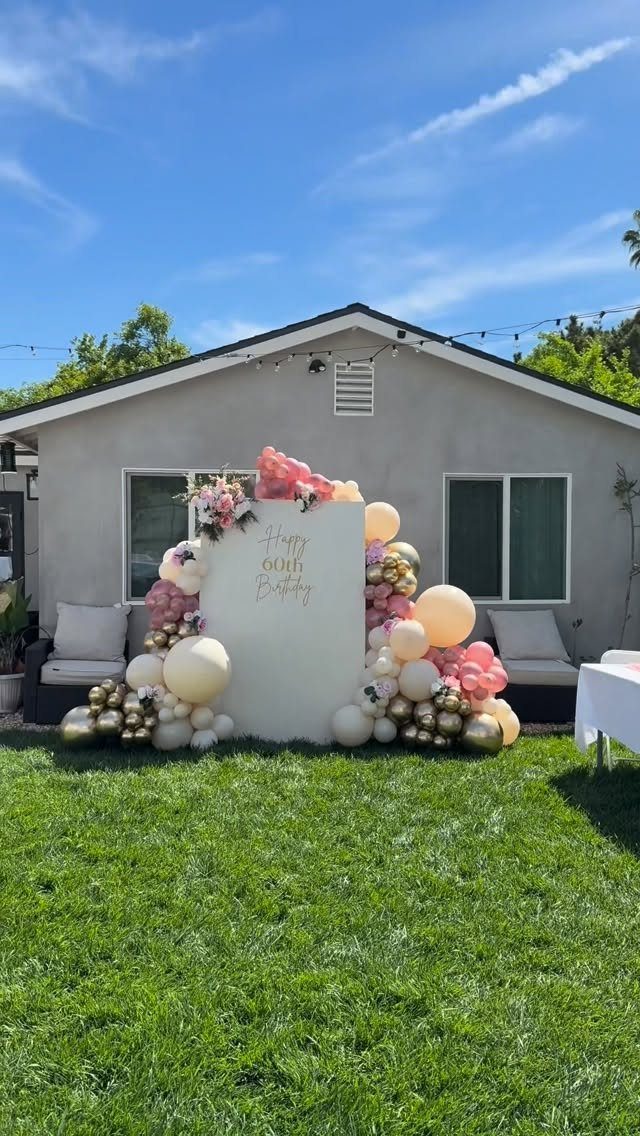 White backdrop framed by pink, gold, and white balloon garlands in a backyard.