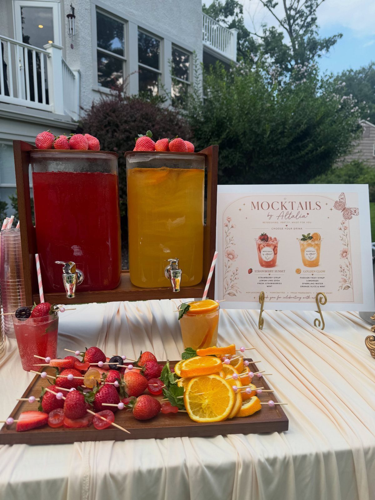 Beverage dispensers with red and yellow drinks and fruit skewers on a table.