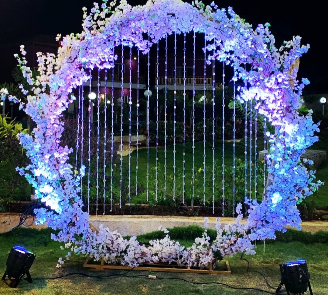 Circular floral arch with blue lighting and hanging crystals on a night lawn