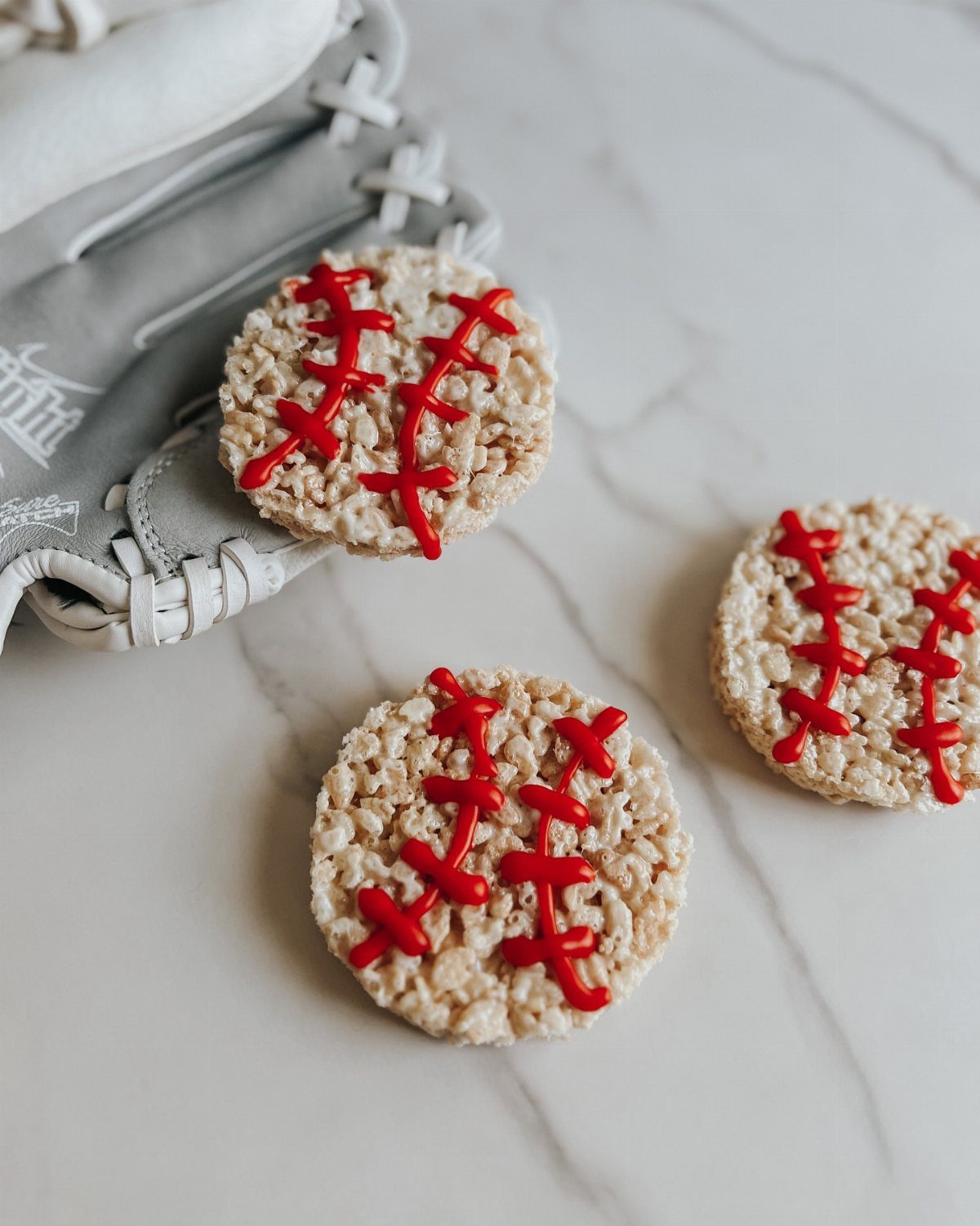 Baseball-shaped rice cereal treats with red icing next to a grey baseball glove.