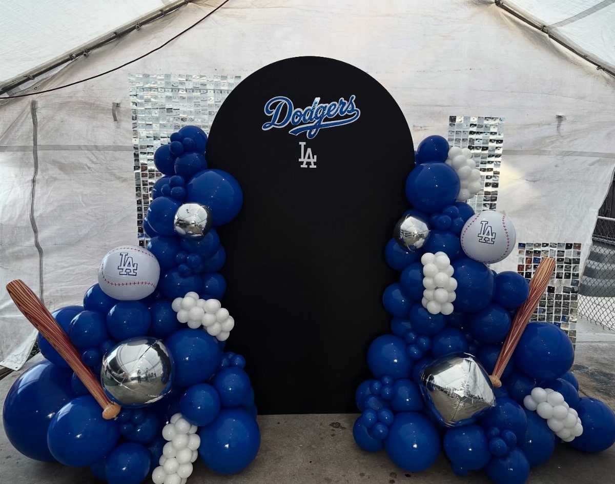 Dodgers themed party backdrop with blue balloon garlands and baseball bats.