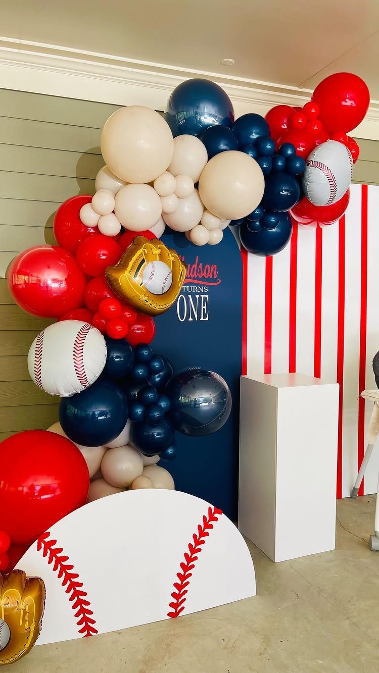 Baseball-themed party decorations with a red, blue, and cream balloon arch and backdrop.