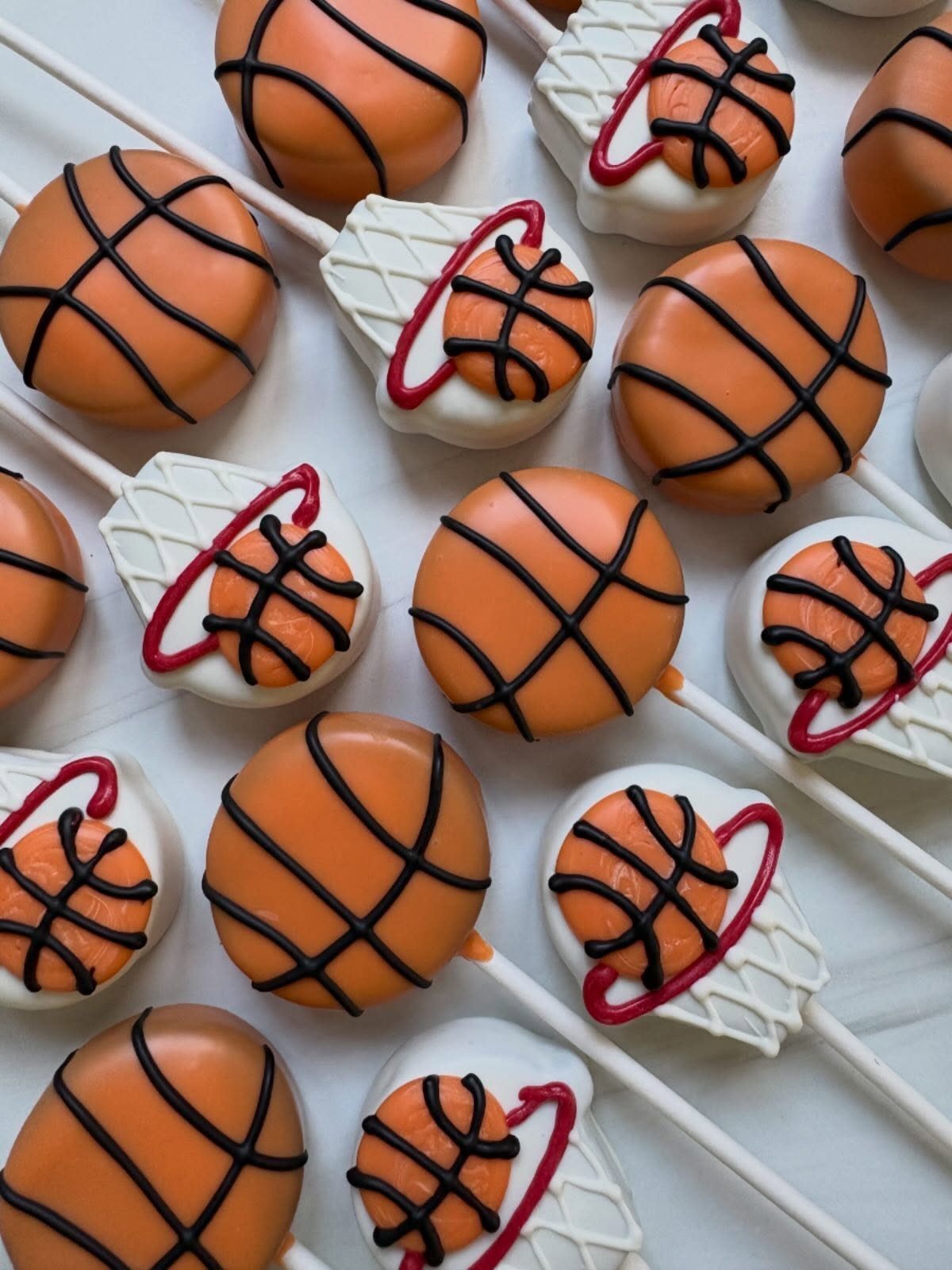 Basketball cake pops with orange frosting and white hoop designs on white sticks.