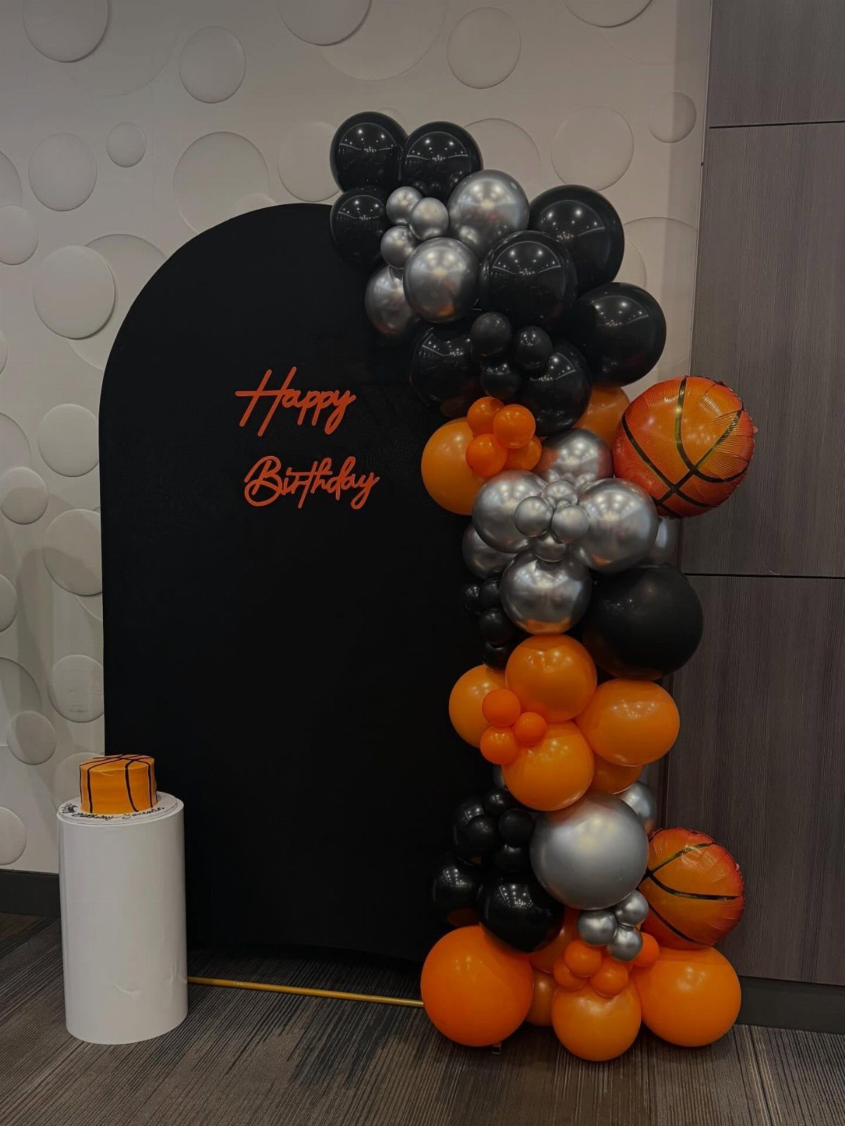 Black birthday backdrop with orange and silver balloon garland and basketball balloons.