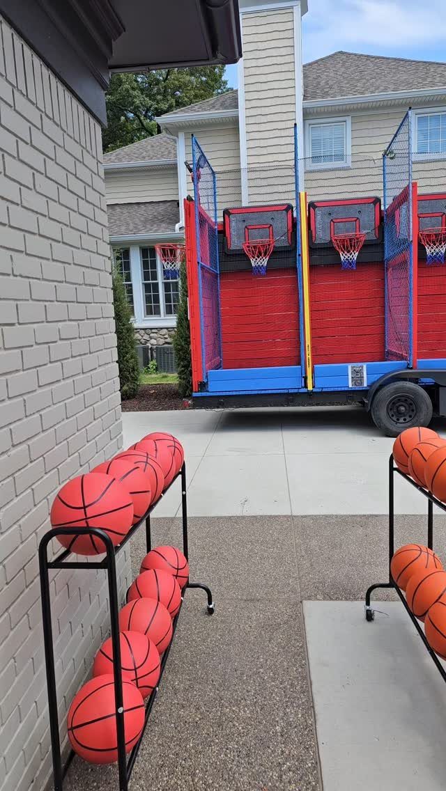 Basketballs on racks in a driveway with a mobile basketball game trailer behind.