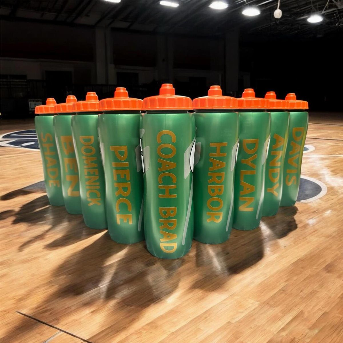 Green sports water bottles with personalized yellow names on a basketball court.
