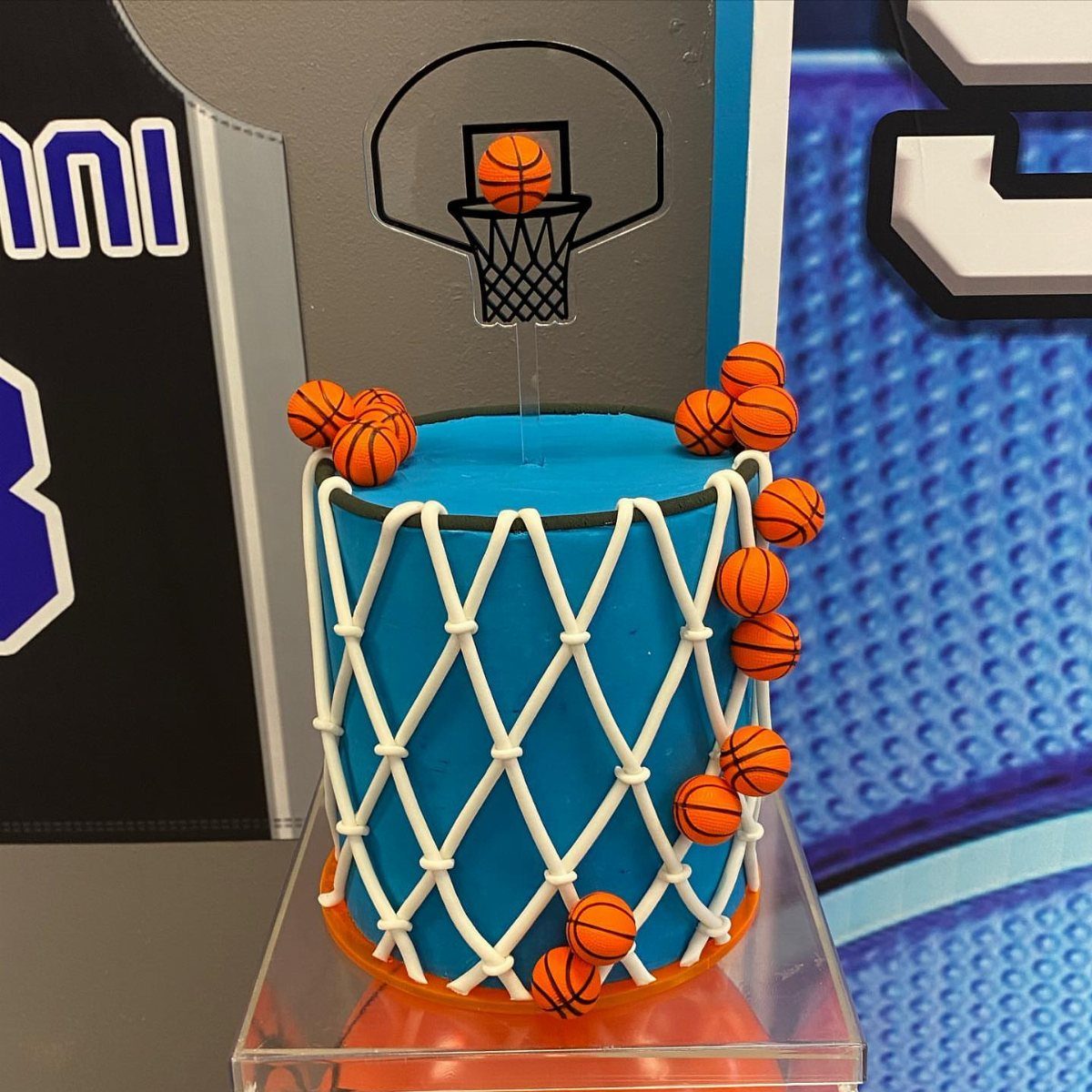 Blue cylindrical cake with white net icing and small orange basketball decorations.