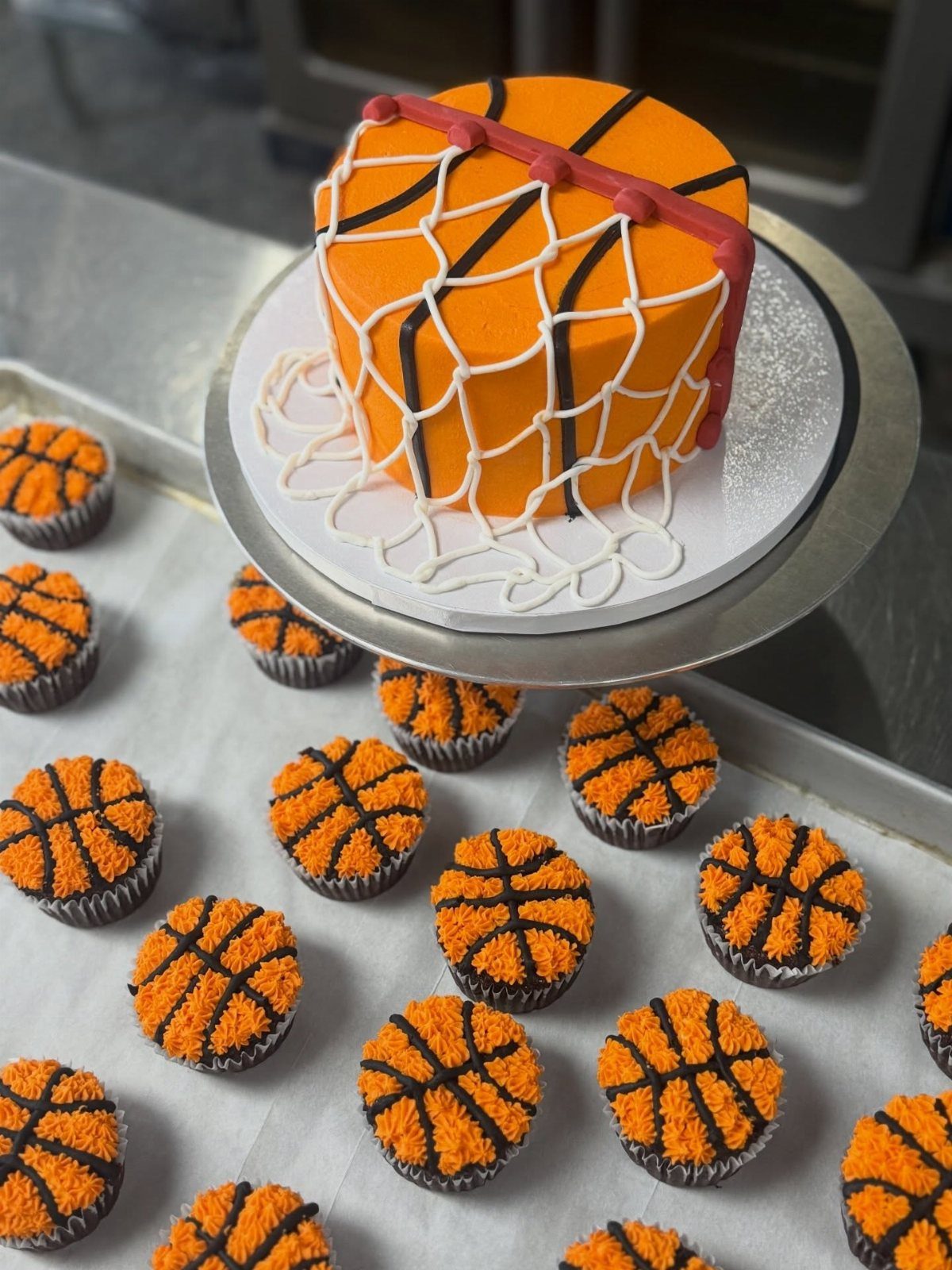 Orange basketball cake with white net frosting surrounded by basketball cupcakes