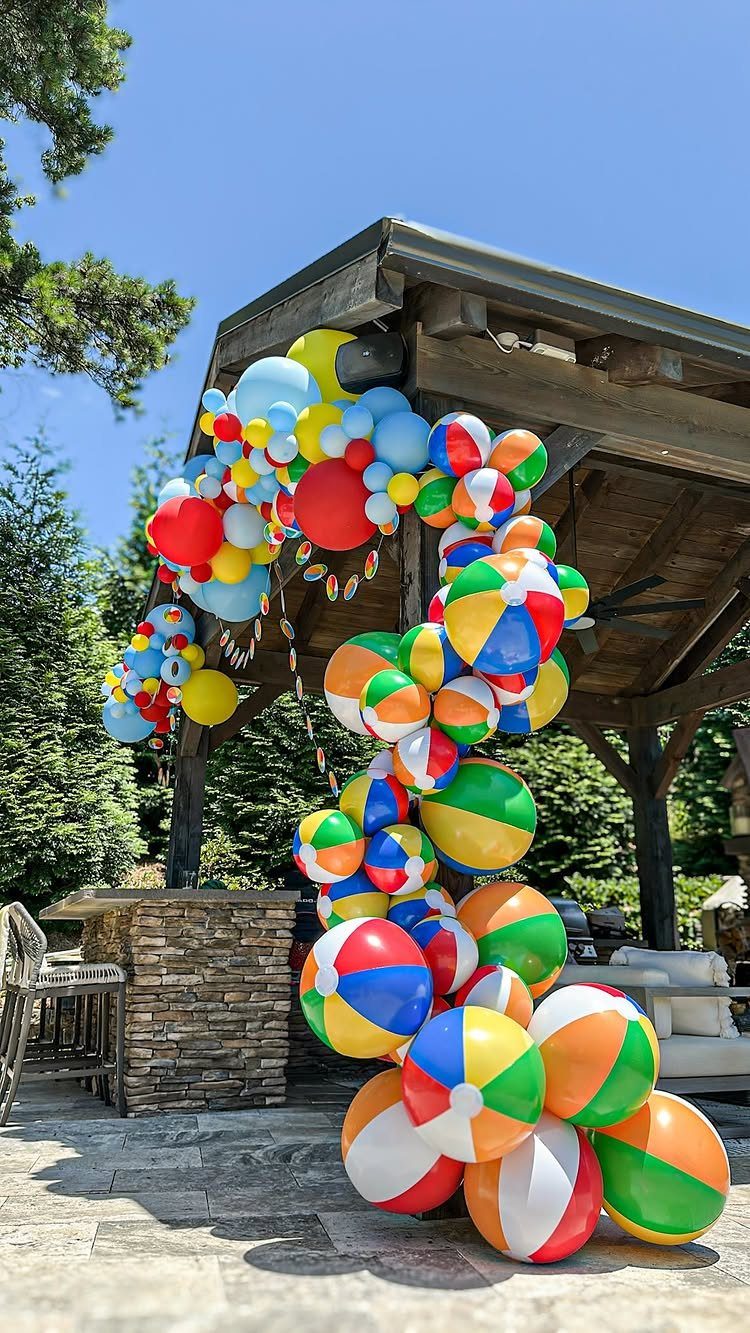 Colorful beach balls and balloons arranged in a decorative arch under a pavilion.