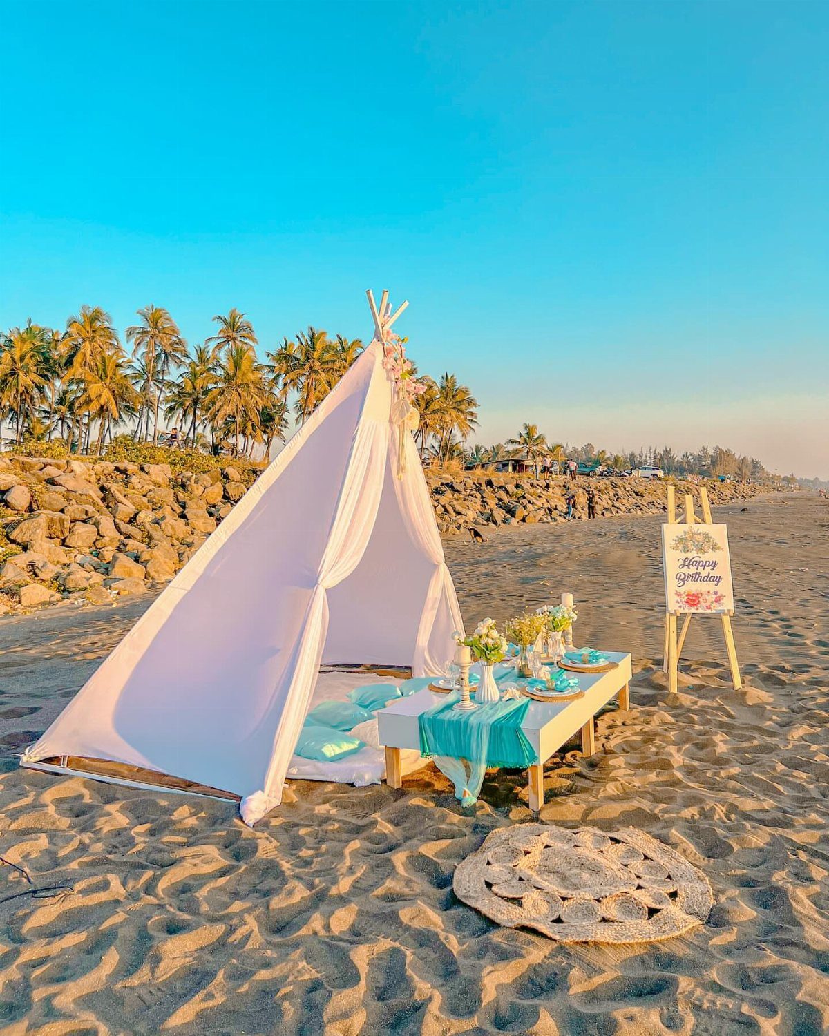 White teepee and low table with turquoise decor on a sandy beach