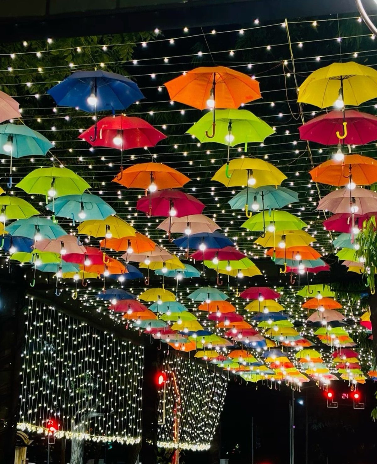 Colorful umbrellas hanging upside down under a canopy of twinkling white fairy lights.