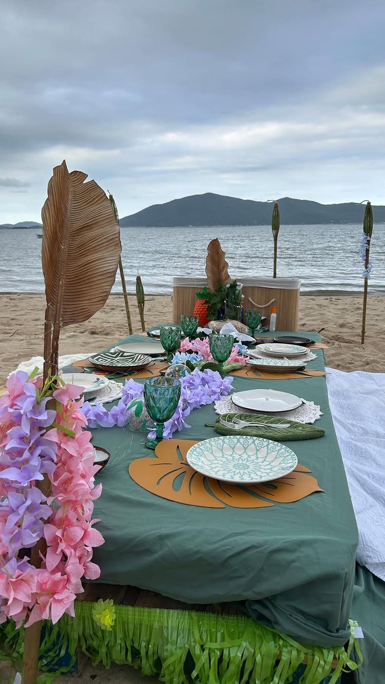 Tropical beach party table setting with green cloth, floral leis, and teal glassware.