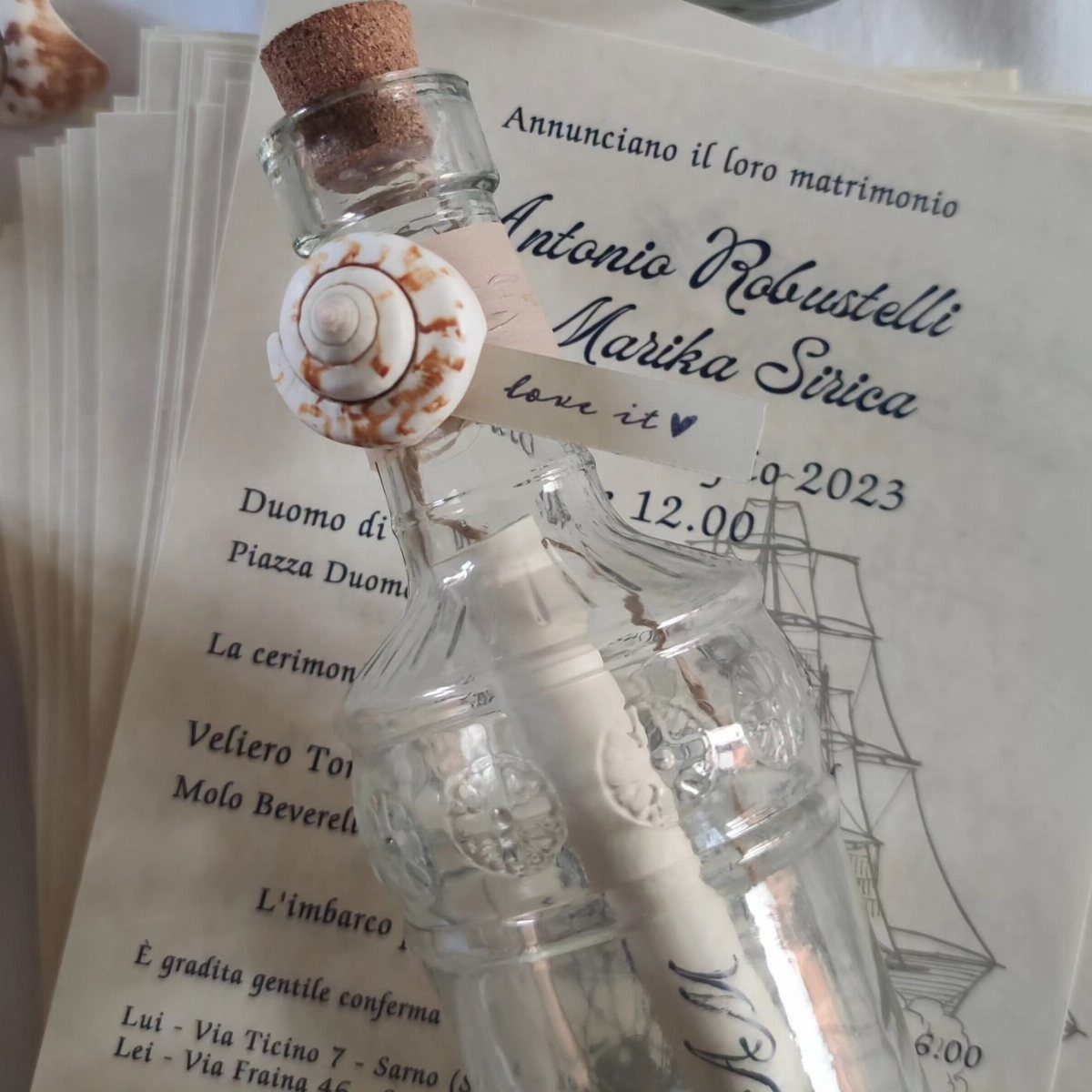 Glass bottle with a rolled scroll and seashell resting on a wedding invitation.