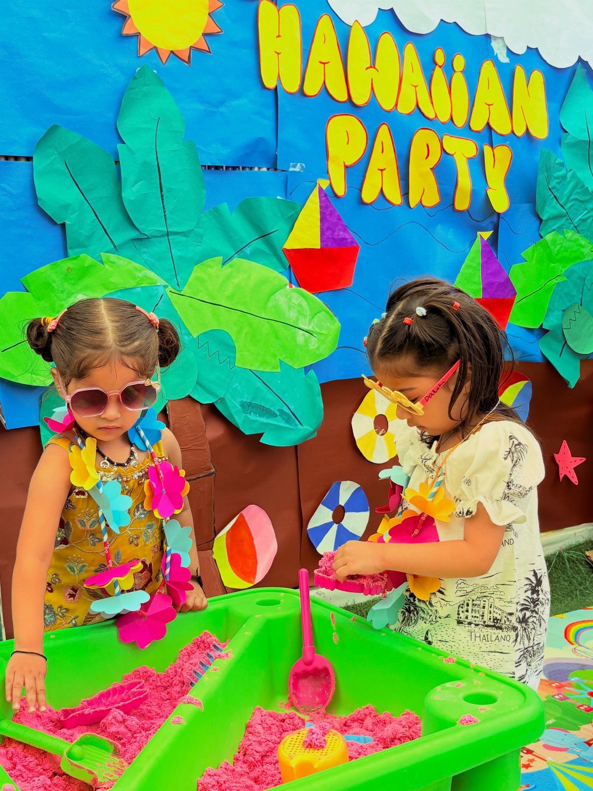 Two girls in leis playing with pink sand at a Hawaiian party.