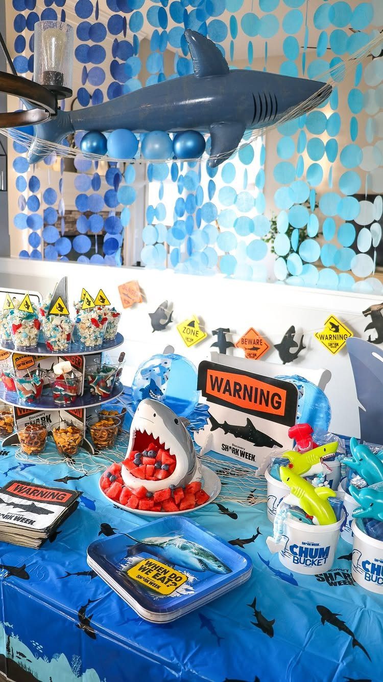 Shark-themed party table with a shark cake, blue decorations, and a hanging shark model.