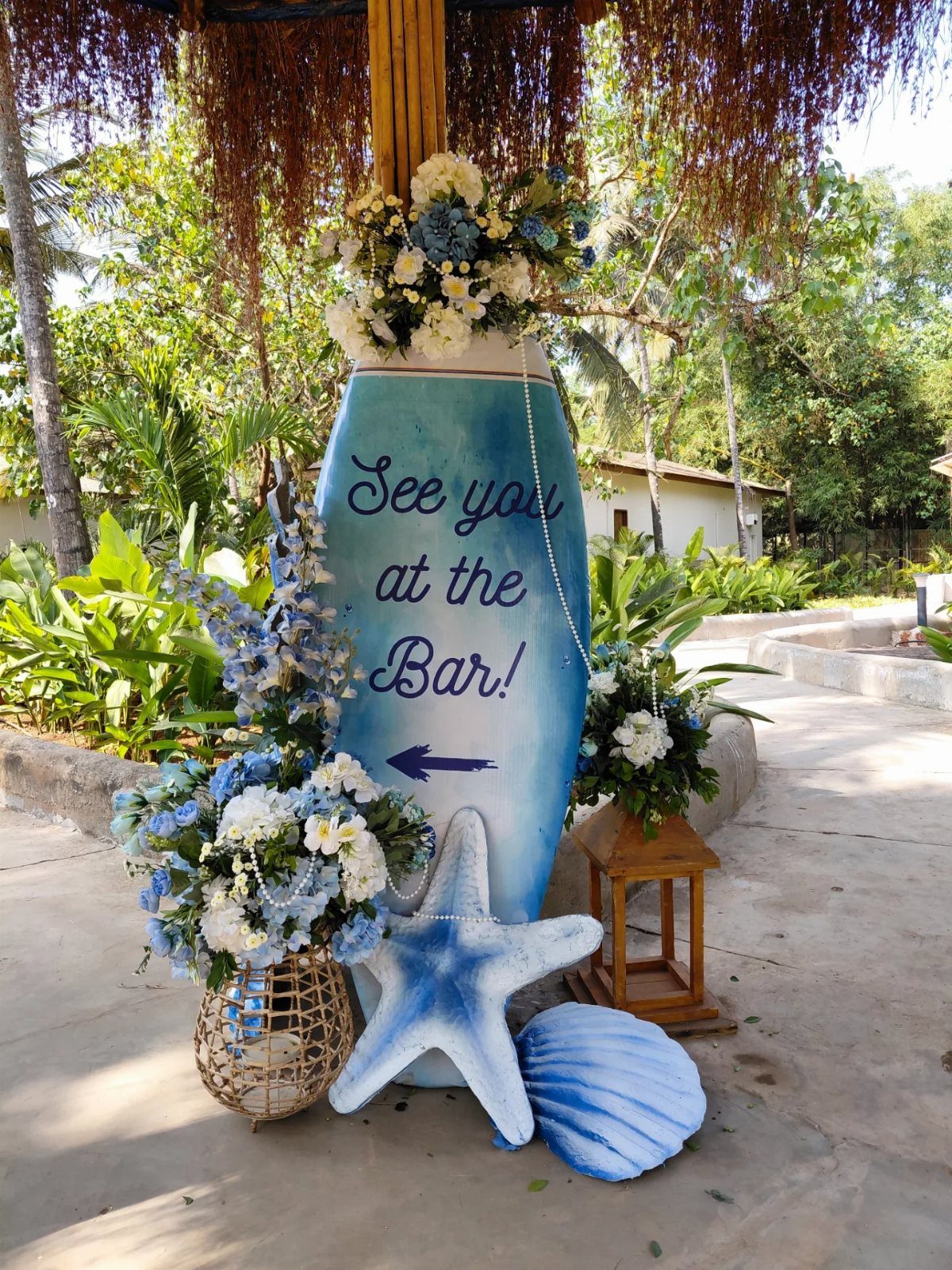 Blue surfboard sign with beach decorations and flowers for a themed party.