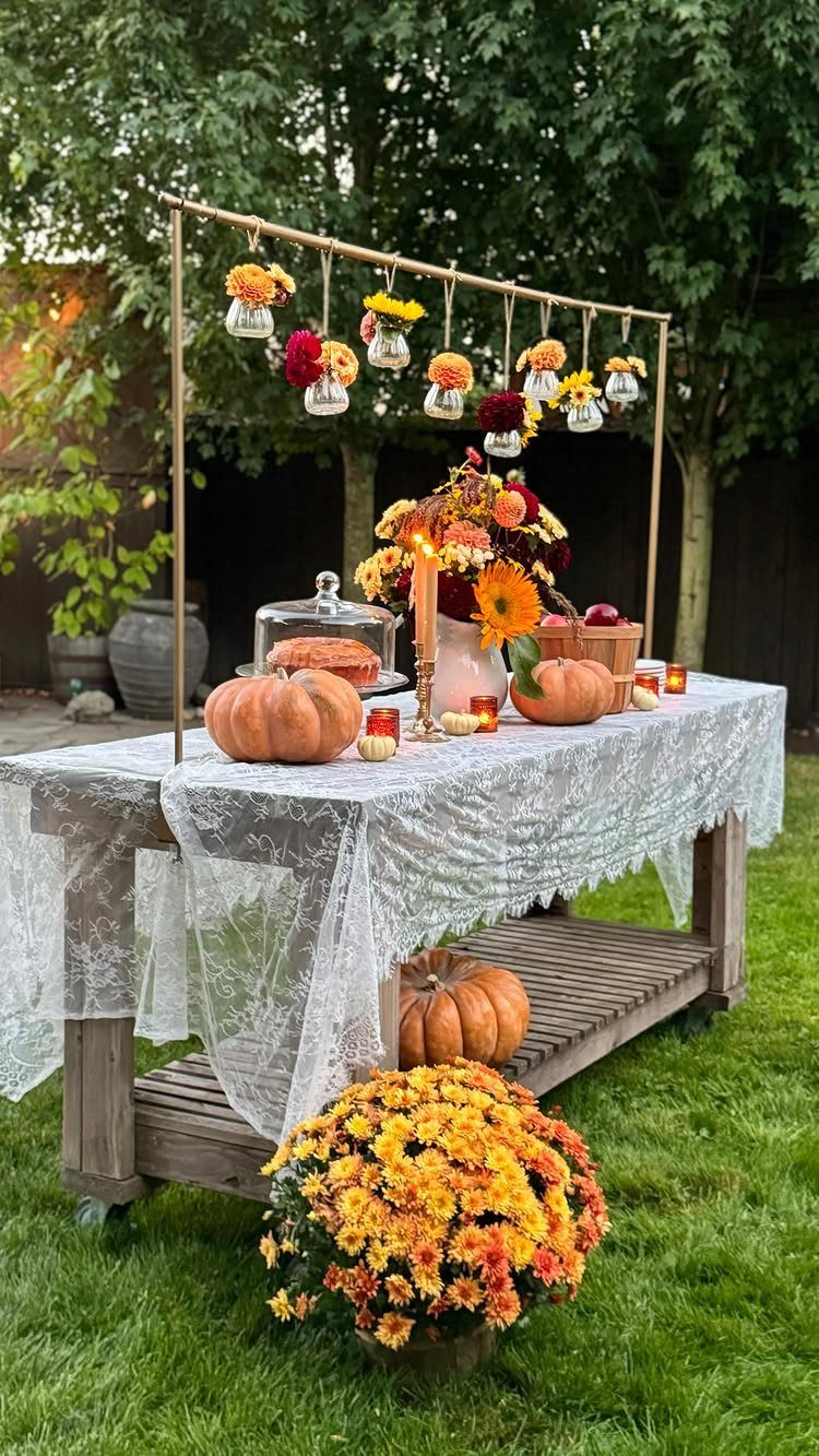 Autumnal celebration table with lace cloth, pumpkins, orange flowers, and hanging floral vases.