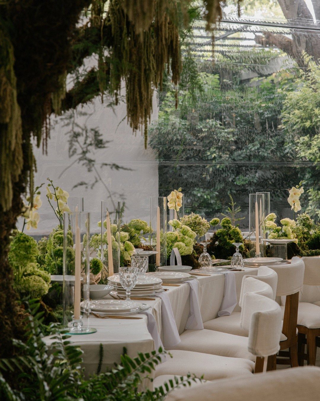 Elegant white dining table with green floral centerpieces and candles in a garden