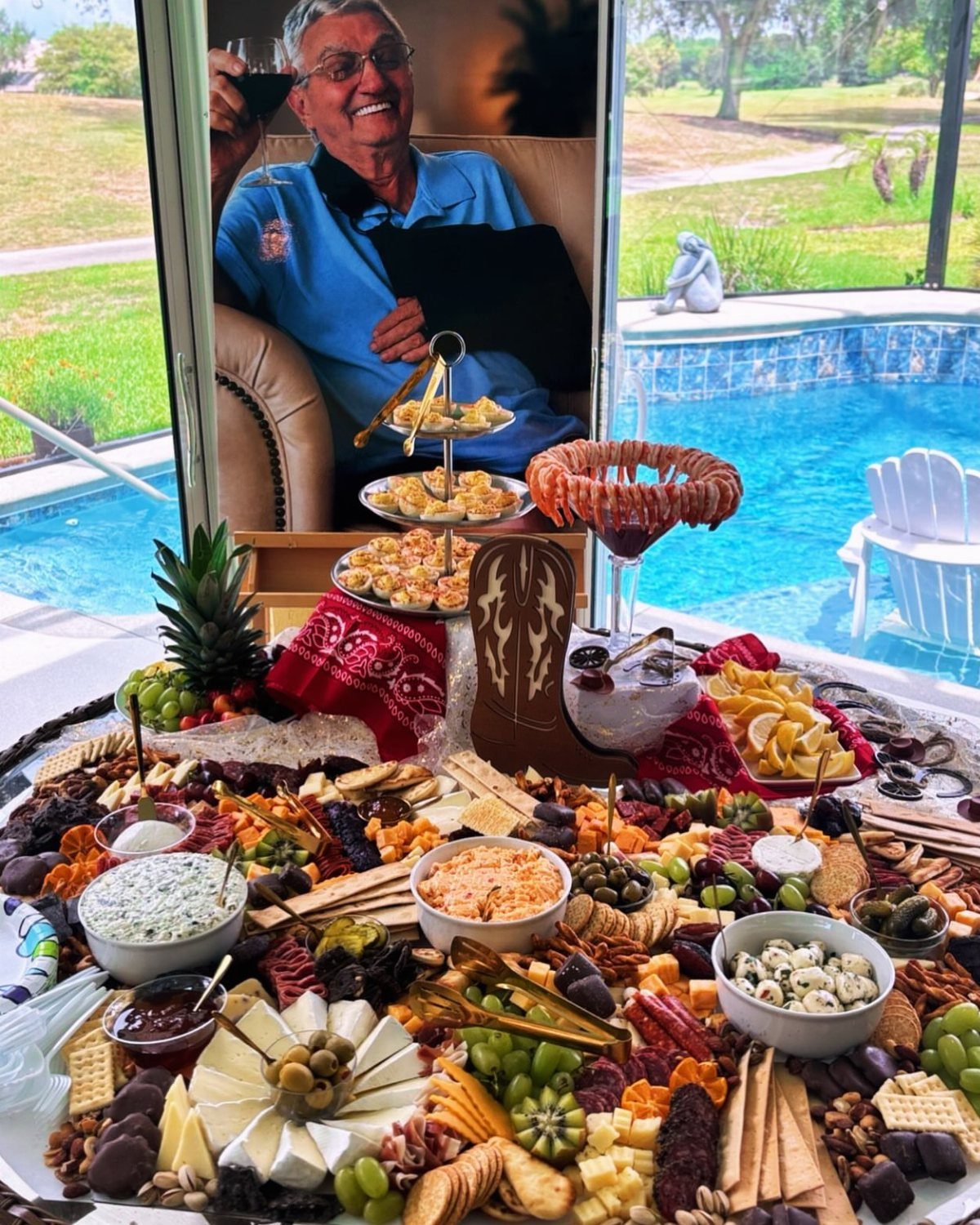 Charcuterie board and appetizers arranged in front of a large memorial portrait by a pool