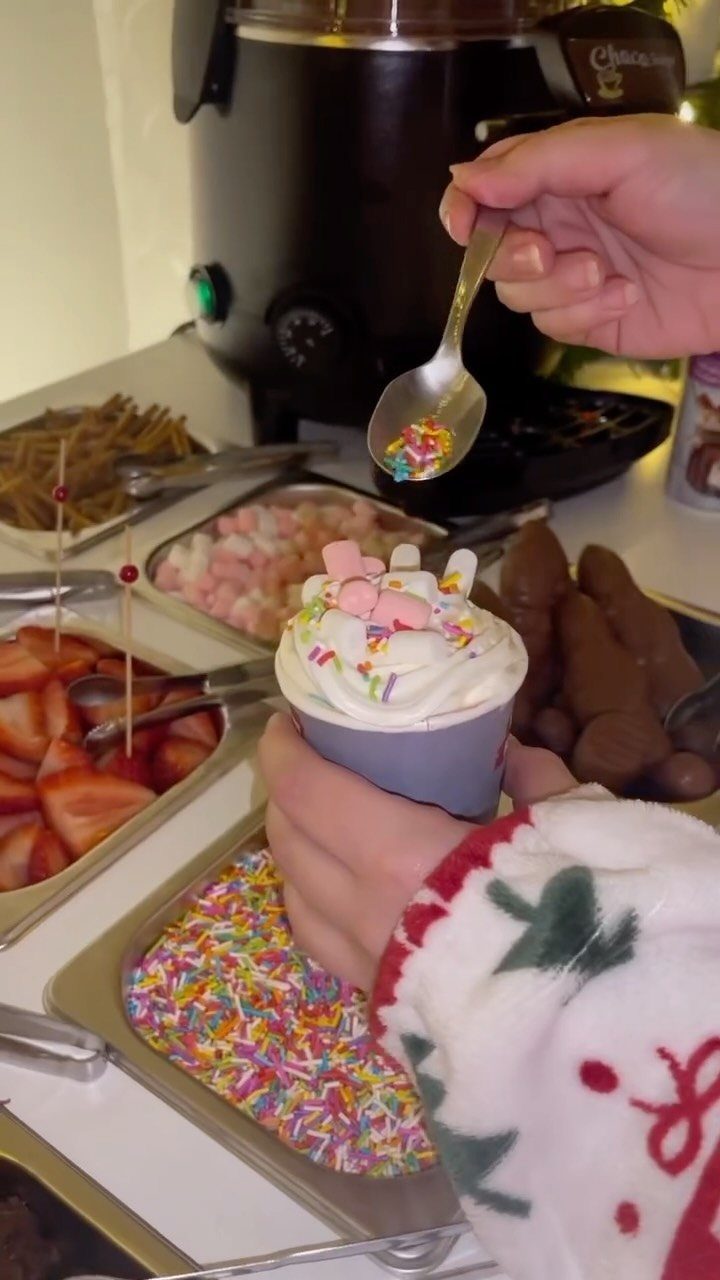 Person adding colorful sprinkles to whipped cream at a Christmas chocolate fountain station