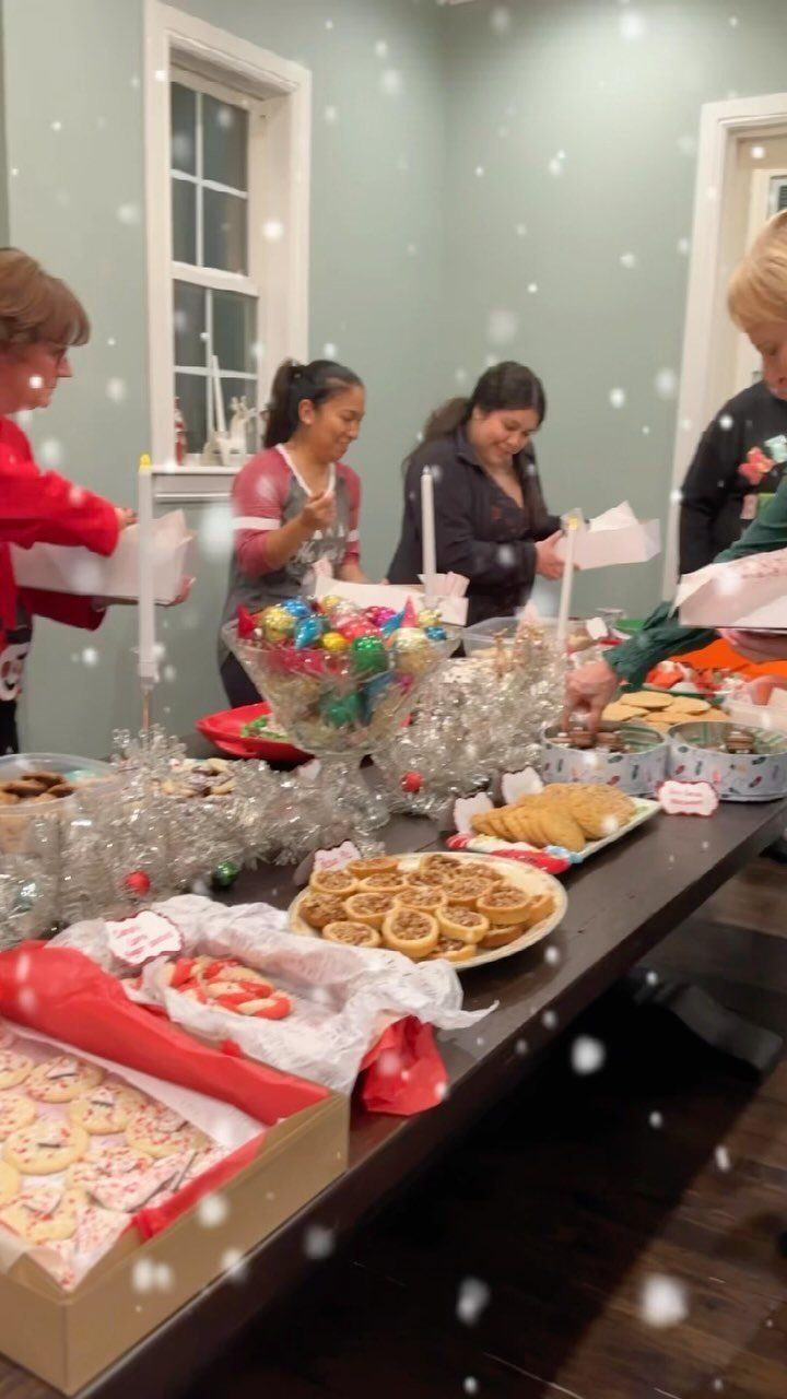 People gathering around a table filled with assorted Christmas cookies and festive treats.