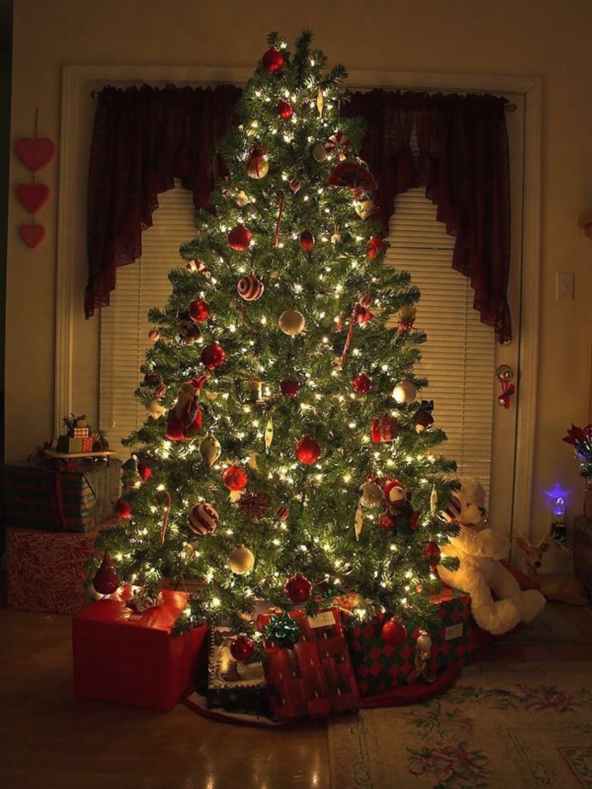 Decorated Christmas tree with glowing lights and red ornaments surrounded by wrapped gifts.