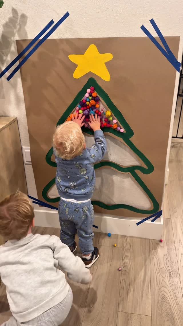 Two young children playing with a DIY paper Christmas tree on a wall