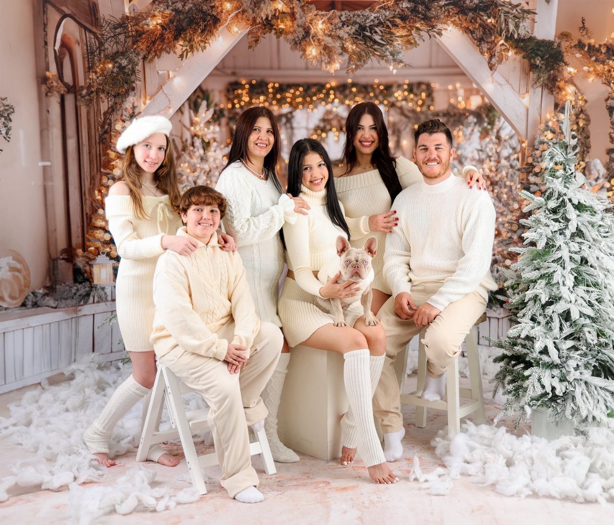 Family in matching cream sweaters posing with a dog in a snowy studio.