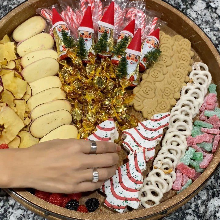Christmas dessert platter with Santa figurines, cookies, and candies being touched by a hand