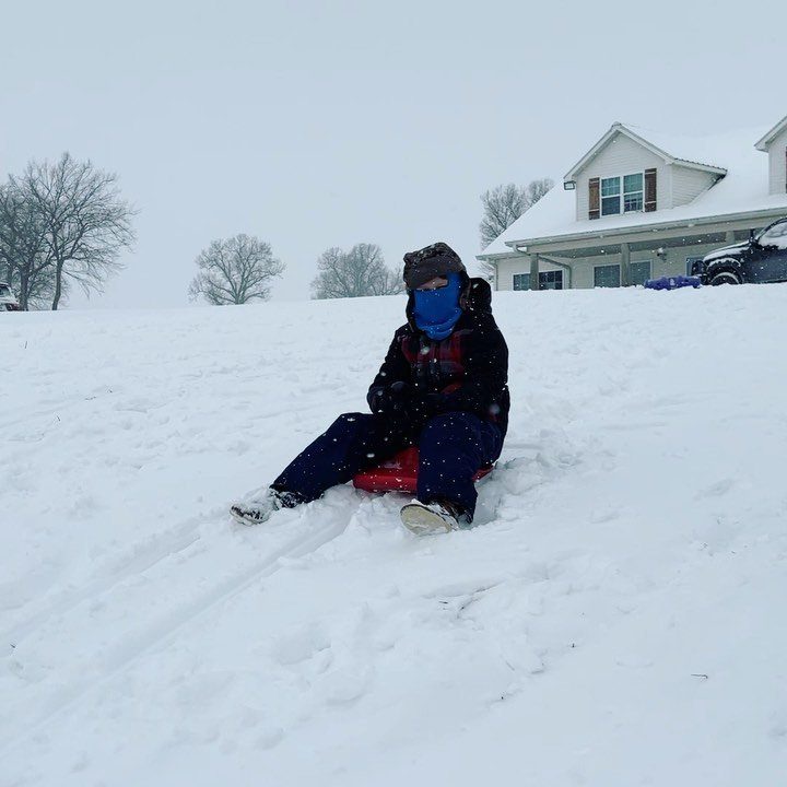 Person on a red sled sliding down a snowy hill near a house