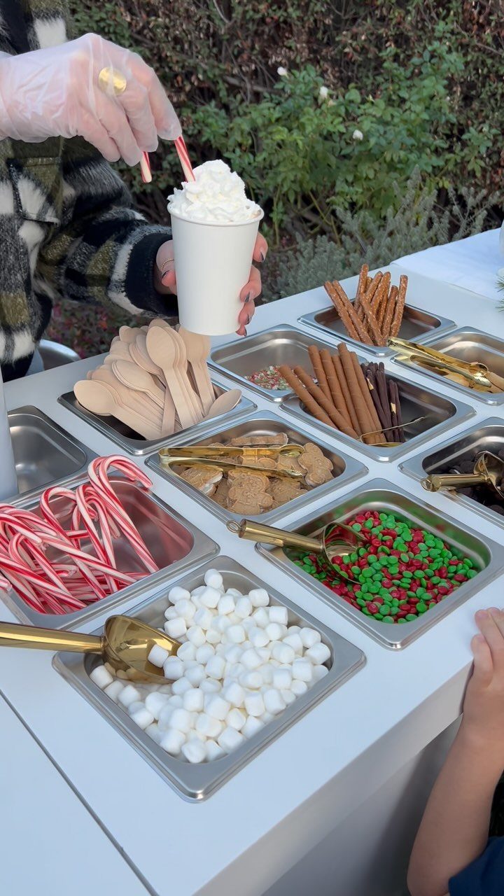 Person holding whipped cream topped drink at a hot chocolate topping station