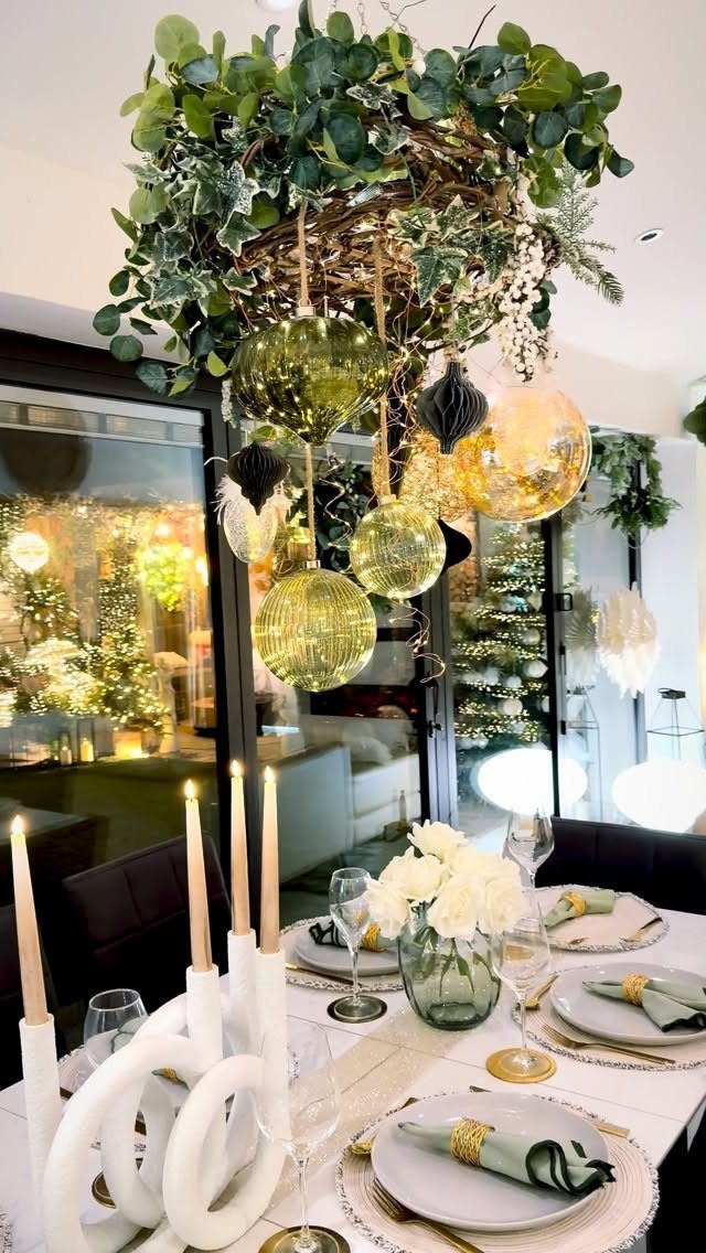 Greenery chandelier with gold ornaments hanging over a decorated white Christmas dining table